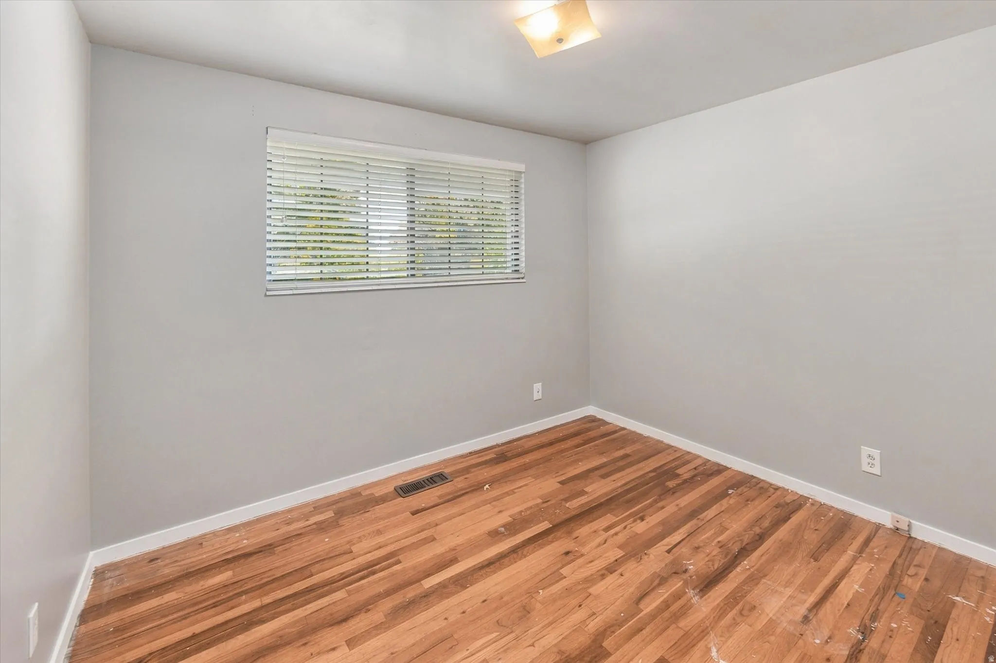 Wood-finish flooring, neutral wall paint, overhead lighting, and a window with blinds