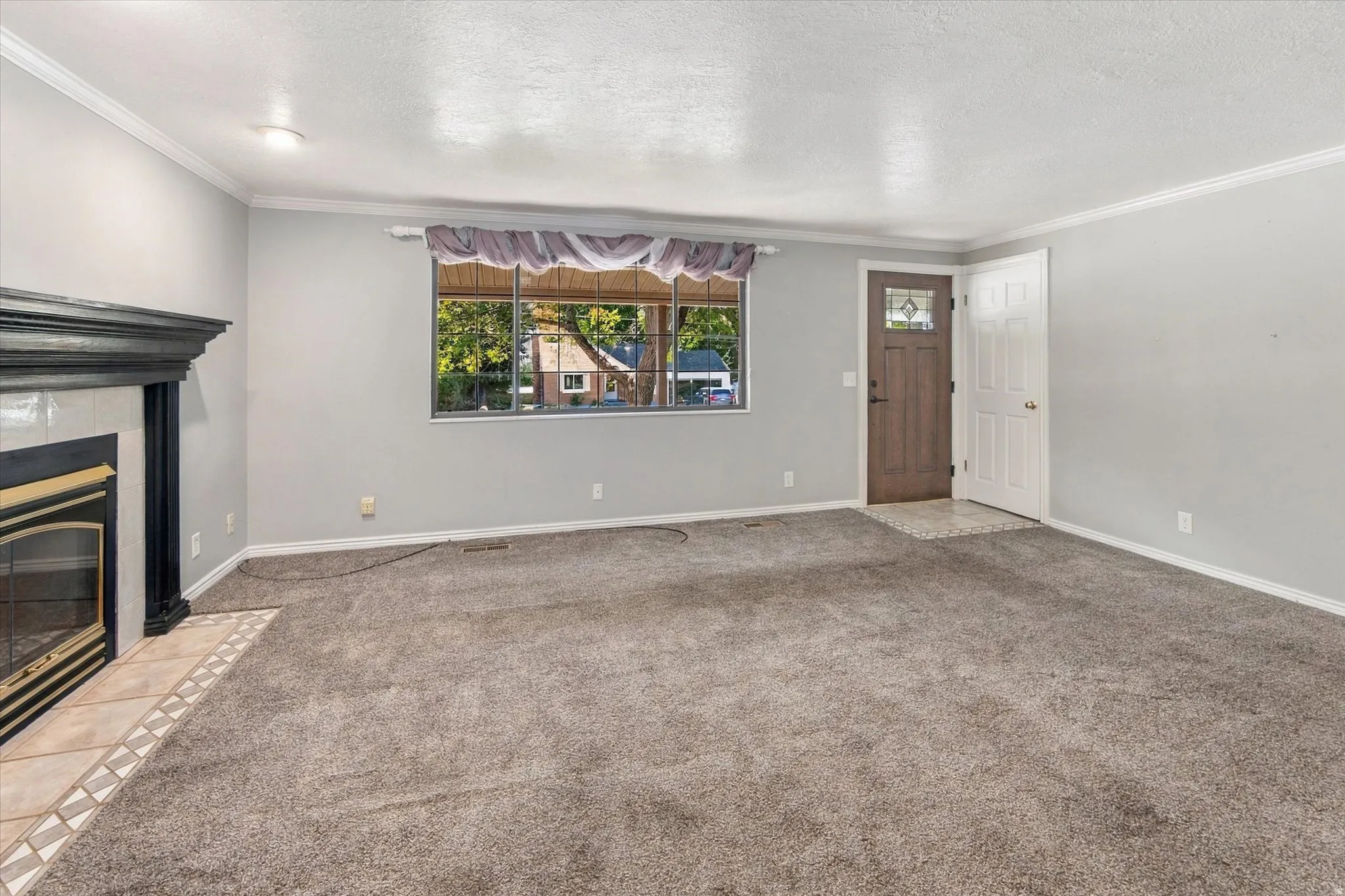 Fireplace with tile surround, carpeted flooring, white crown molding, light gray wall paint, and a wood-paneled entry door with frosted glass detailing