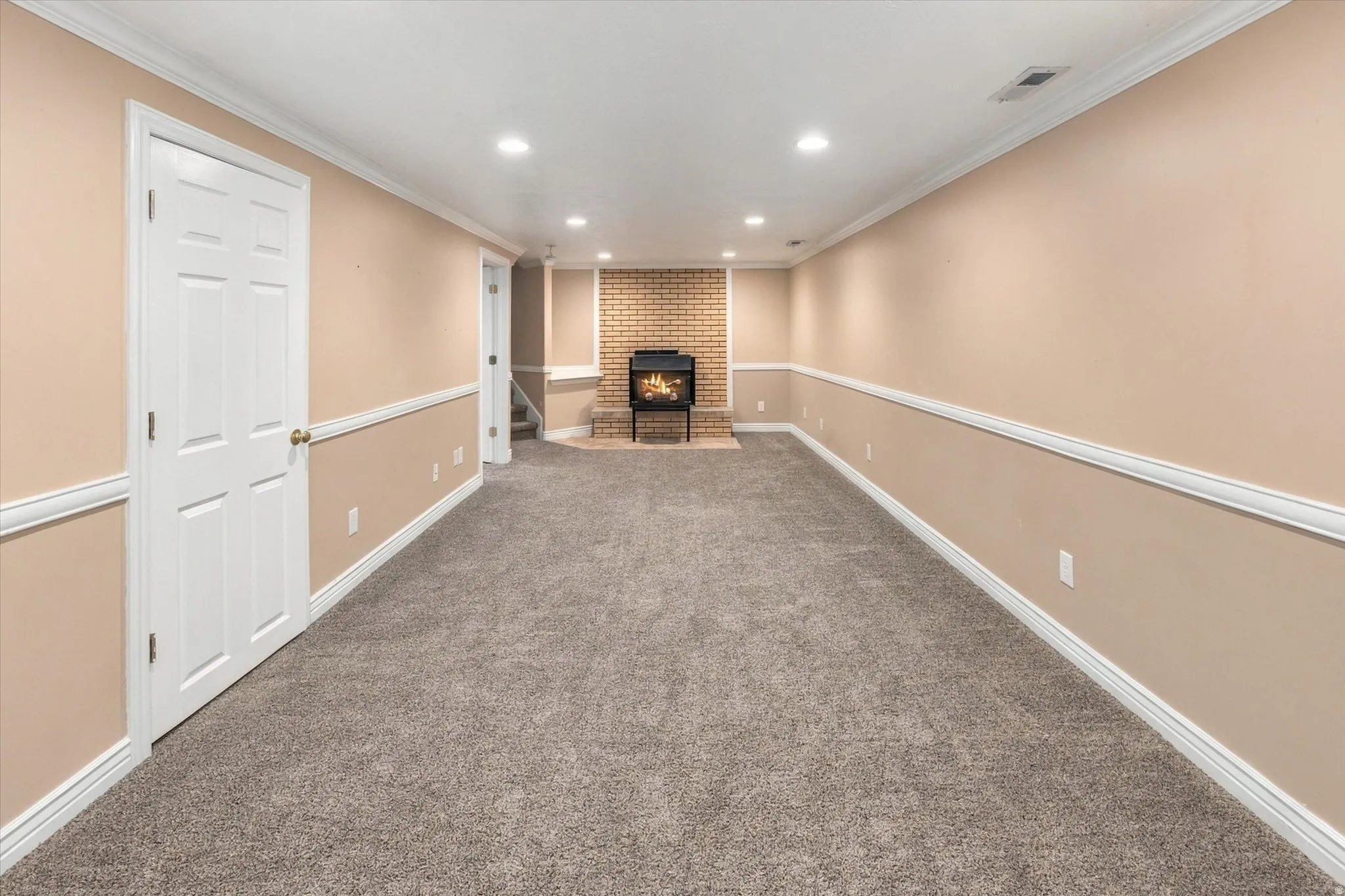 Spacious room featuring neutral carpeting, a brick fireplace, wainscoting, and recessed lighting