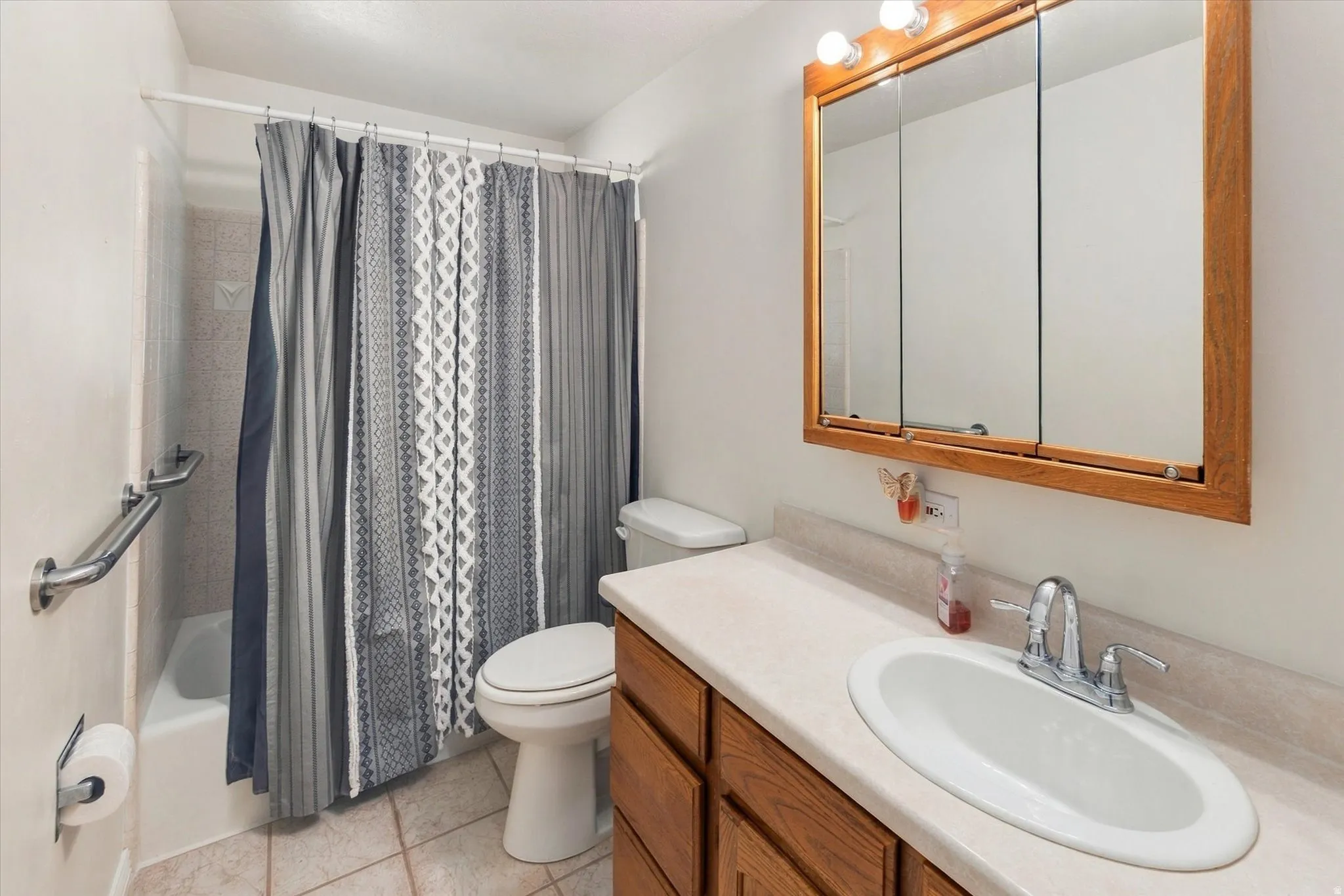 Bathroom with a shower-over-tub combination, tiled flooring, wood-finish vanity with an integrated sink, and an overhead medicine cabinet
