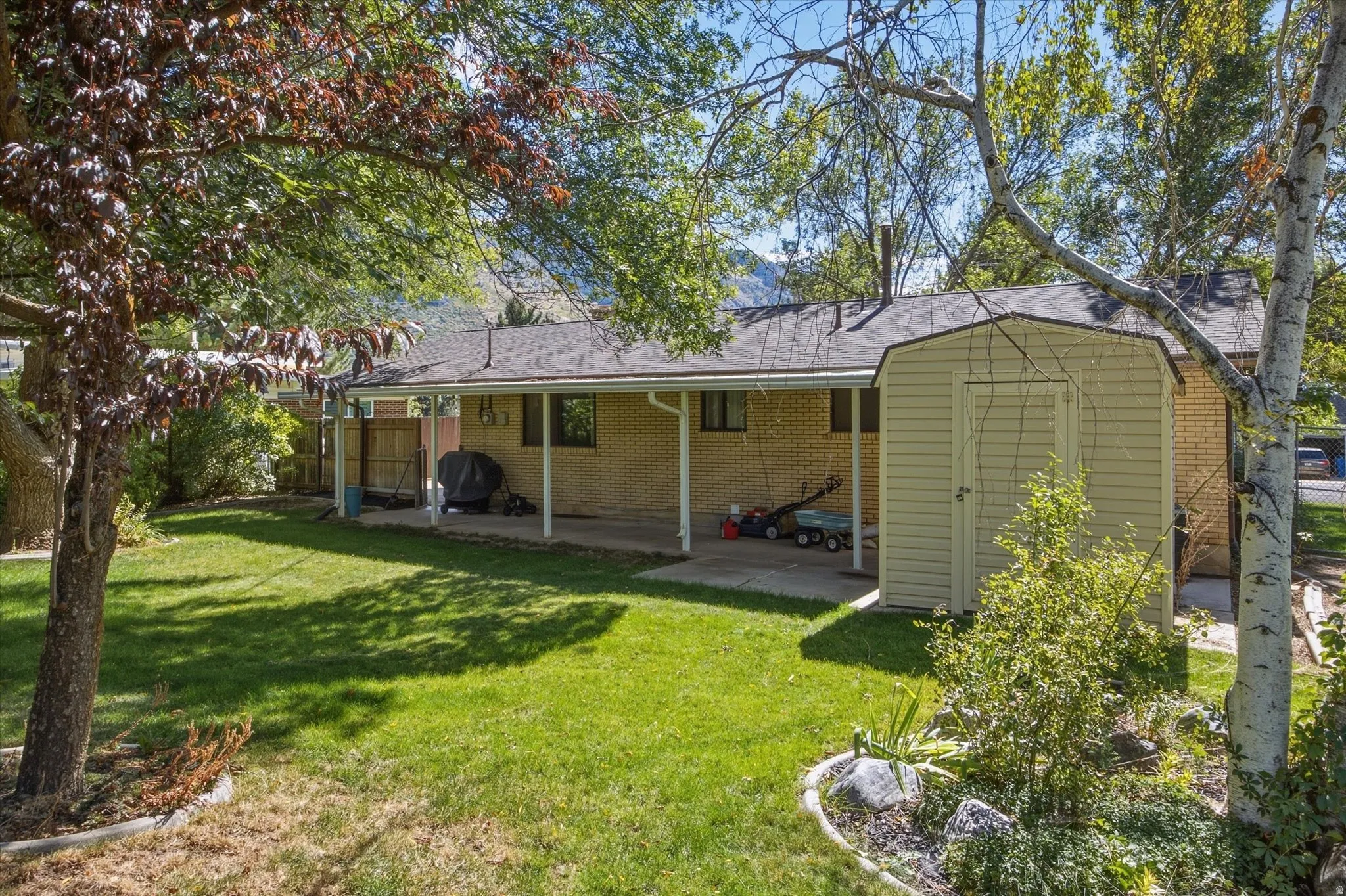 Expansive backyard featuring a manicured lawn, established trees, and a covered patio