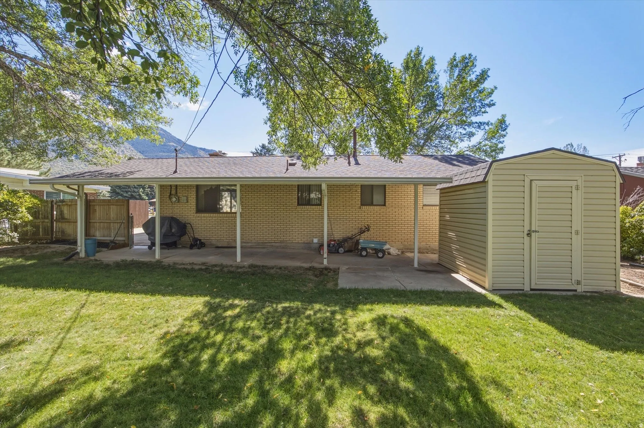 Expansive backyard with a covered patio, manicured lawn, and a storage shed