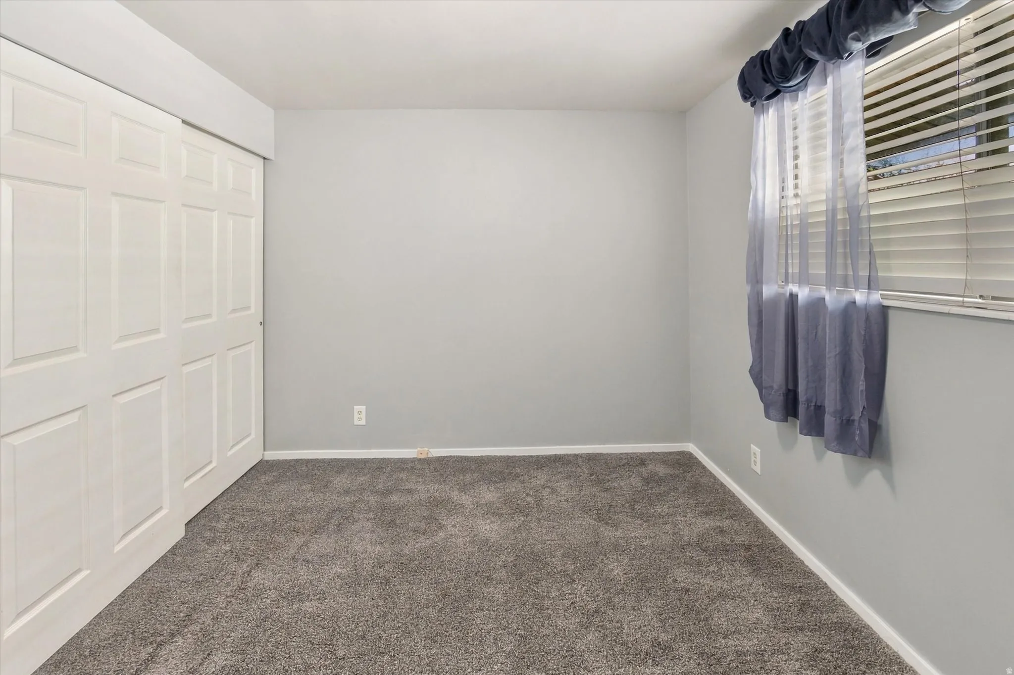 Soft gray wall paint, textured gray carpeting, white bi-fold closet doors, and white window blinds