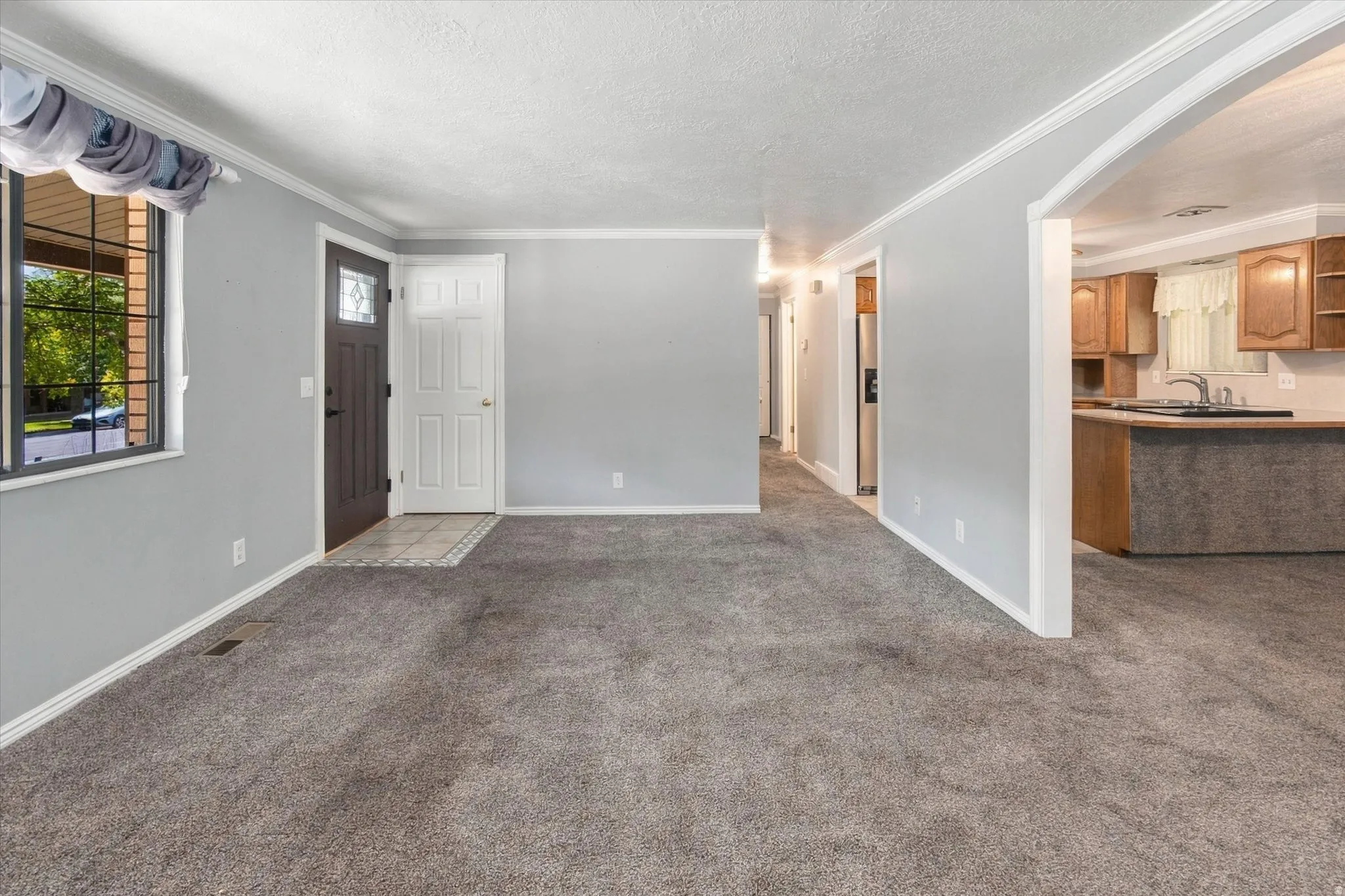 Spacious room with gray carpeting, an arched doorway, and an entryway with tile flooring