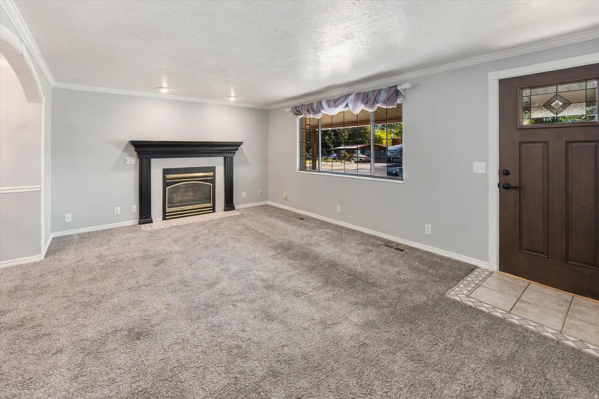 Arched doorway, fireplace with dark wood surround, recessed ceiling lighting, light gray walls, and a wood entry door with decorative glass inserts