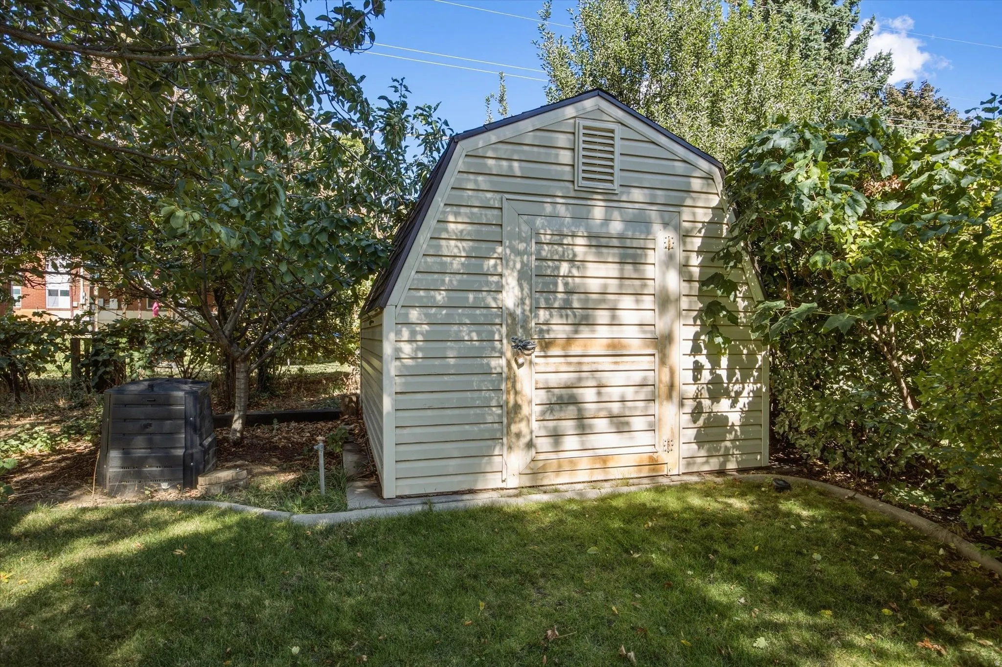 Gable-roof storage shed with horizontal siding, set on a concrete pad, surrounded by mature trees and landscaping