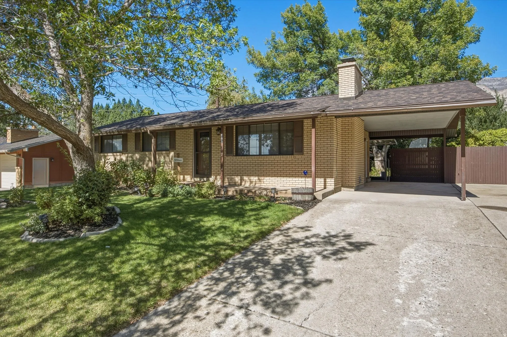 Brick exterior with a covered carport, attached chimney, and a concrete driveway