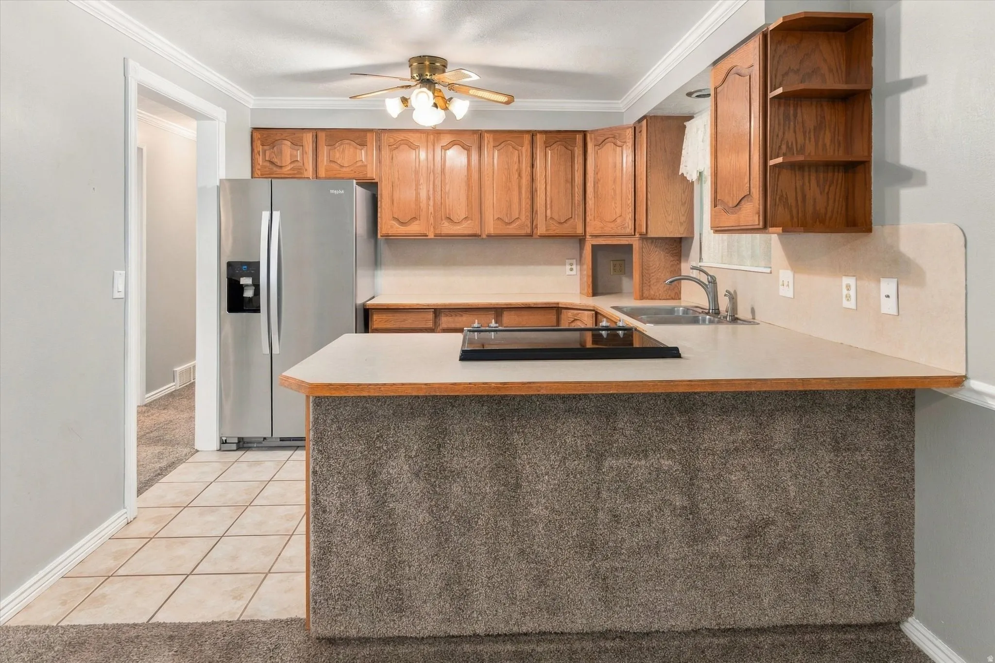 Wood-finish cabinetry, built-in stainless steel refrigerator, integrated cooktop, stainless steel sink, and ceiling fan with light fixture