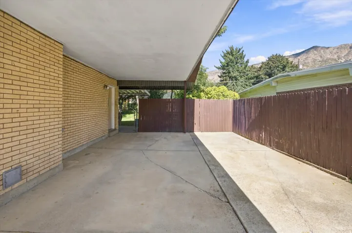 Covered carport with a concrete slab, brick exterior, wood privacy fence, and mountain backdrop