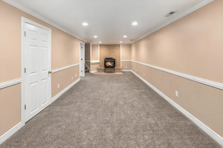Spacious room featuring neutral carpeting, a brick fireplace, wainscoting, and recessed lighting