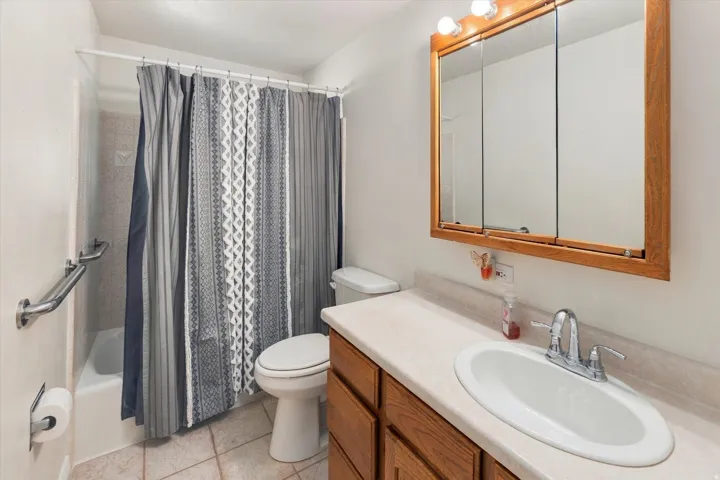 Bathroom with a shower-over-tub combination, tiled flooring, wood-finish vanity with an integrated sink, and an overhead medicine cabinet