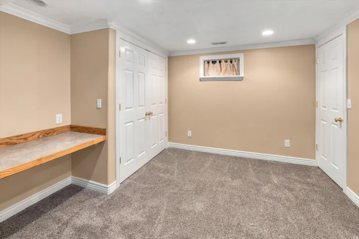 Built-in desk surface with wood-finish trim, dual paneled closet doors, recessed lighting, and crown molding