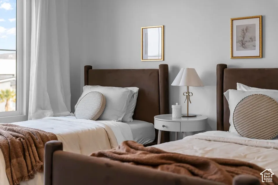 Window with white trim, light gray walls, brown upholstered headboards, and a white round nightstand with a drawer