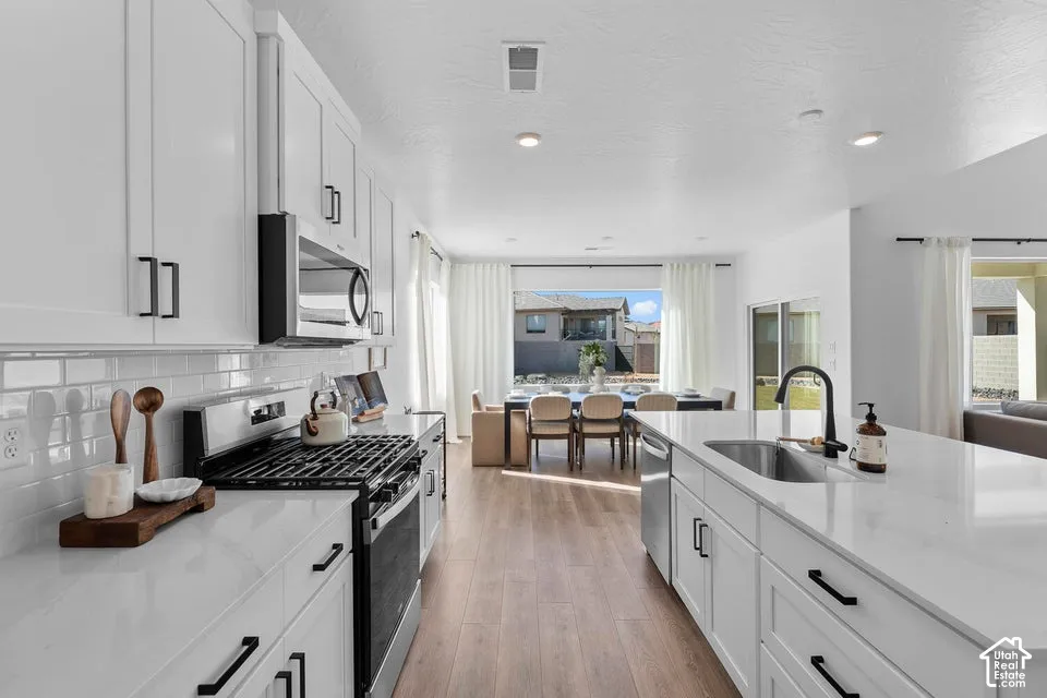 White shaker cabinetry with black hardware, stainless steel appliances, light wood-finish flooring, and white countertops