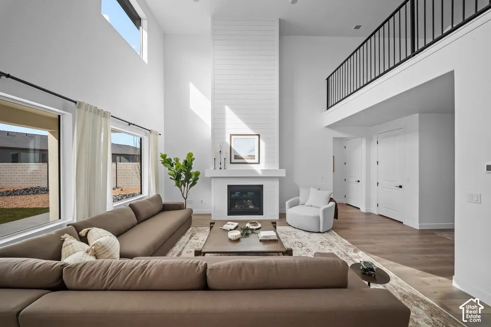Two-story living area featuring a fireplace with shiplap surround, wood-finish flooring, high ceilings, and an upper-level railing