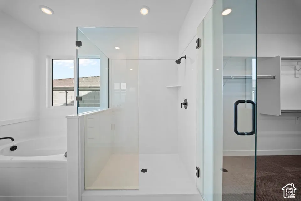 Spa-inspired primary bathroom featuring a frameless glass-enclosed shower with dual showerheads, white subway tile surround, a soaking tub with deck-mounted fixtures, recessed ceiling lighting, and abundant natural light from an oversized window framing r