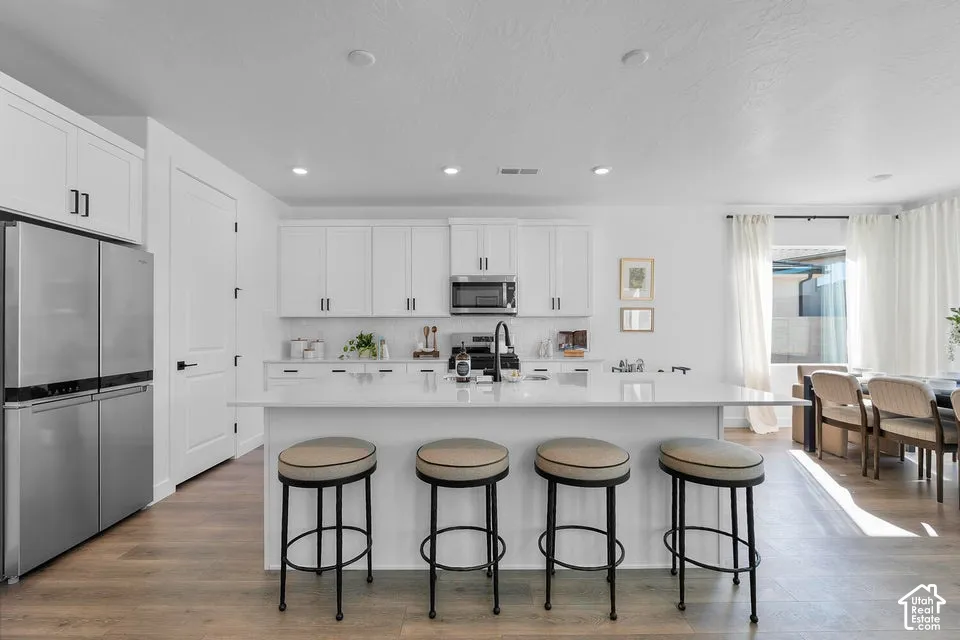 Kitchen featuring white shaker cabinetry, stainless steel appliances, a center island with countertop seating, and wood-finish flooring