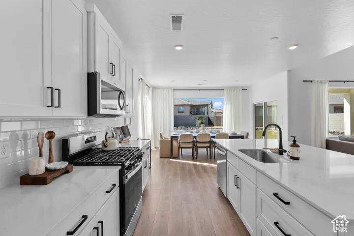 White shaker cabinetry with black hardware, stainless steel appliances, light wood-finish flooring, and white countertops