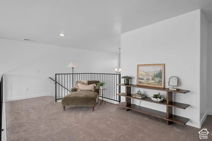 Carpeted loft area featuring a dark wood-finish console table, recessed lighting, and a black metal railing