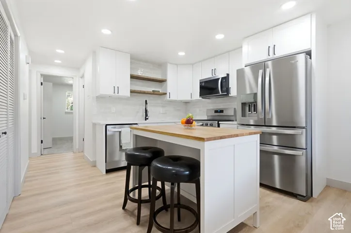 Kitchen featuring wood-finish flooring, white cabinetry, stainless steel appliances, a center island with a wood countertop, and a tile backsplash