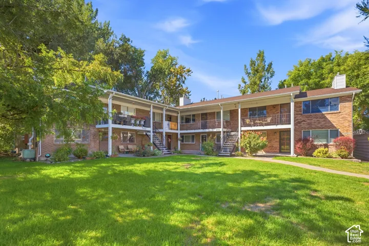 Brick exterior building featuring multiple balconies and patios, surrounded by mature trees and a broad lawn