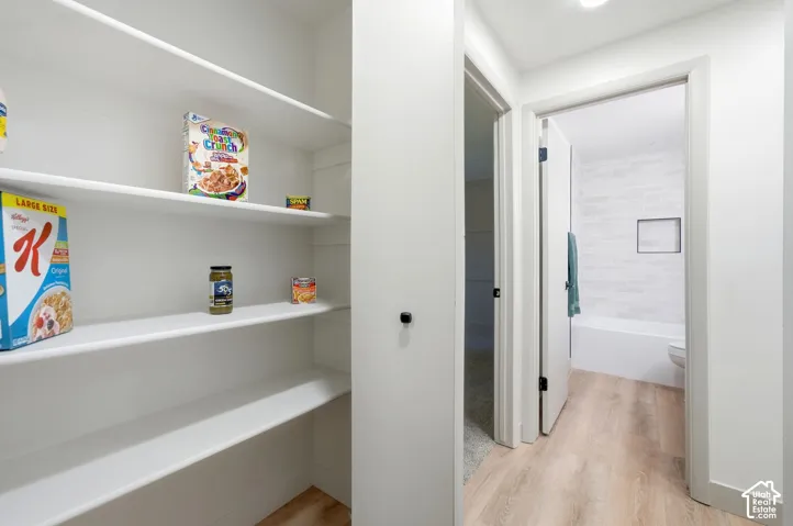 Built-in pantry shelving, wood-finish flooring, recessed lighting, and a modern bathroom with a tiled shower niche and white bathtub