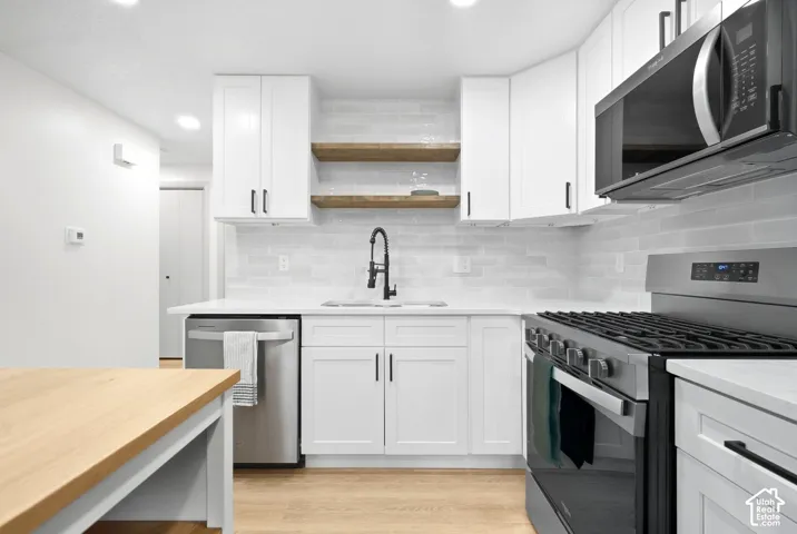 Kitchen featuring white shaker cabinetry, stainless steel appliances, a tile backsplash, wood-finish flooring, and recessed lighting