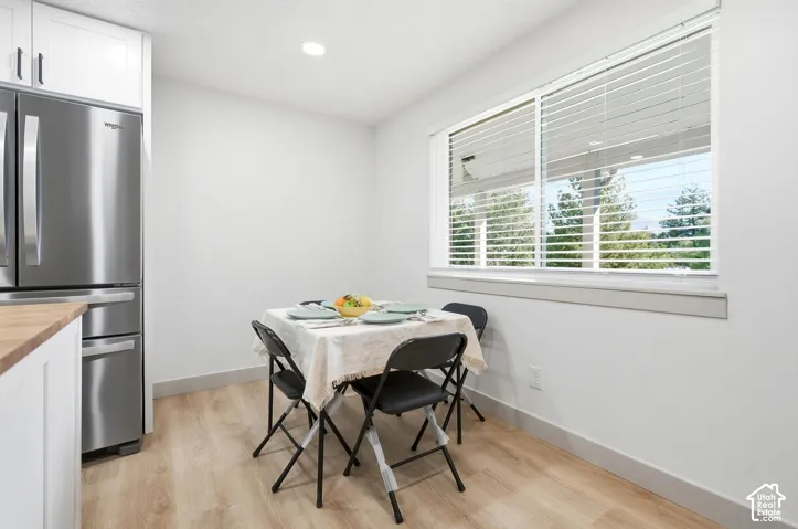 Stainless steel refrigerator, white cabinetry with dark hardware, wood-finish countertop, recessed lighting, and a large window with blinds