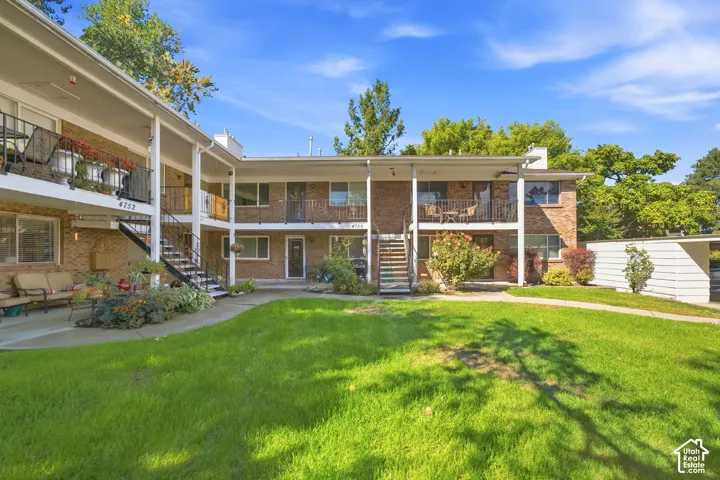 Two-story brick exterior building with multiple balconies, covered walkways, and mature landscaping