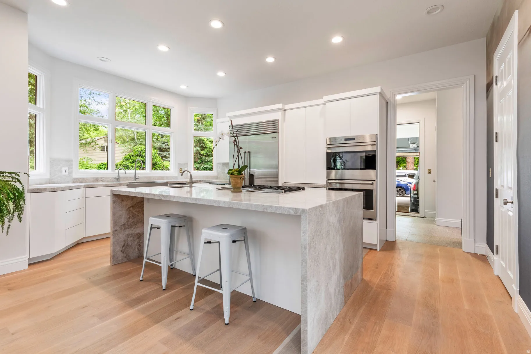 Gourmet kitchen featuring a large central island, light wood-finish flooring, white cabinetry, stainless steel appliances, and abundant natural light from multiple windows