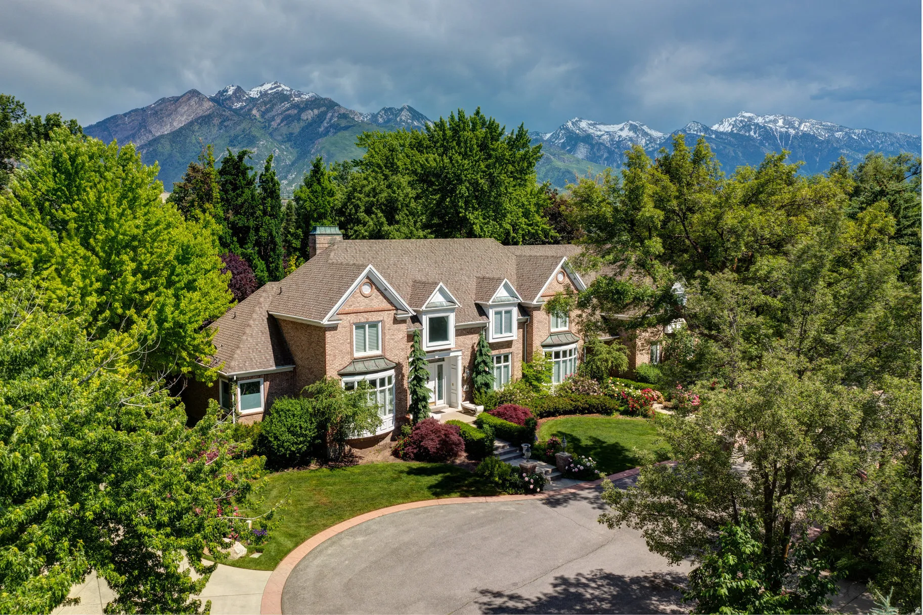 Brick exterior with bay windows and dormers, surrounded by mature trees and landscaping, with a mountain backdrop