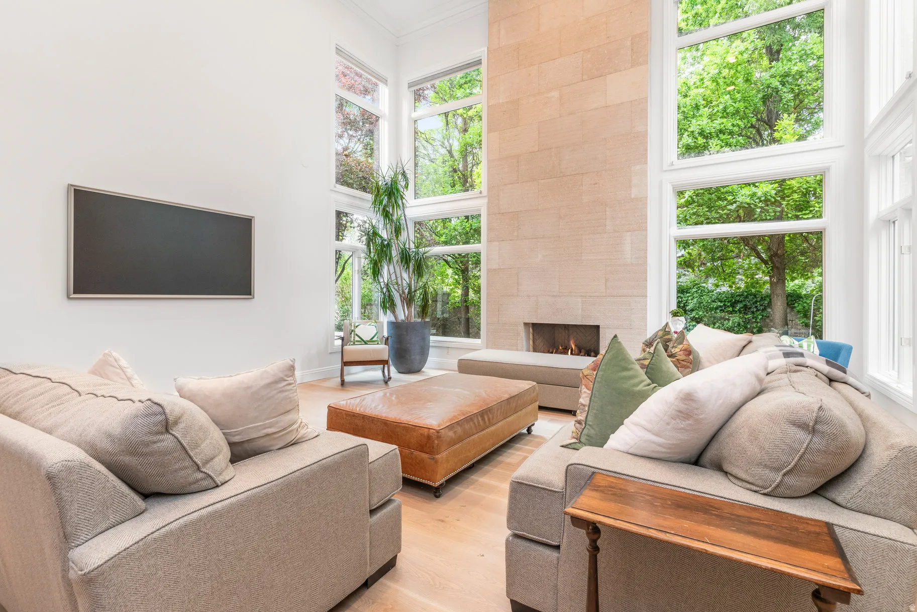 Soaring ceilings with extensive window arrays, stone-clad fireplace with a linear firebox, light-toned wood-finish flooring, and crisp white walls