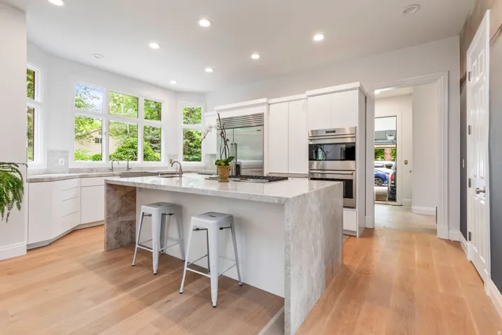 Gourmet kitchen featuring a large central island, light wood-finish flooring, white cabinetry, stainless steel appliances, and abundant natural light from multiple windows