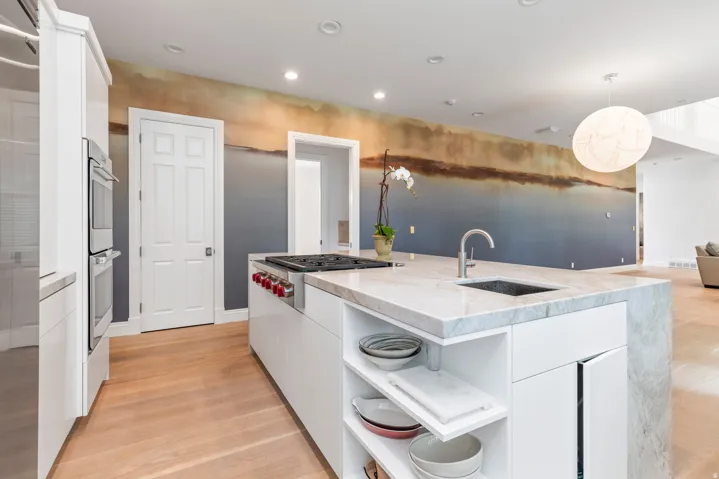Kitchen featuring a stone-clad island with integrated sink, gas cooktop, double wall ovens, and wood-finish flooring