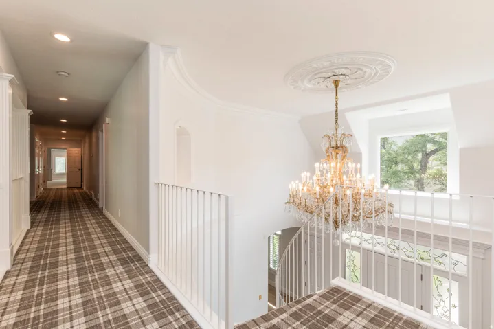 Ornate chandelier with decorative ceiling medallion, extensive crown molding, white painted balusters, and plaid carpeted flooring