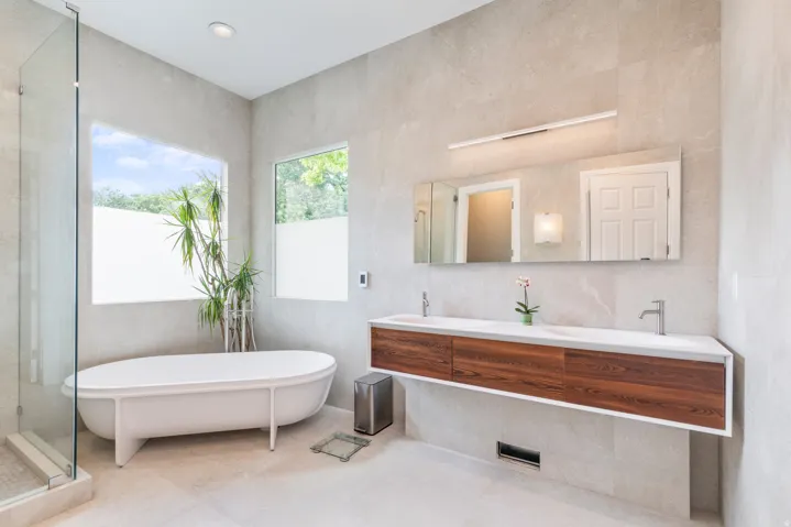 Modern bathroom featuring a freestanding tub, glass-enclosed shower, wood-finish floating double vanity, and large format wall and floor tiling