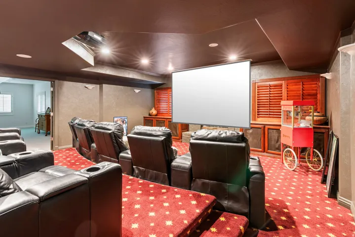 Dedicated media room featuring tiered seating, a large projection screen, recessed lighting, and built-in cabinetry with louvered doors