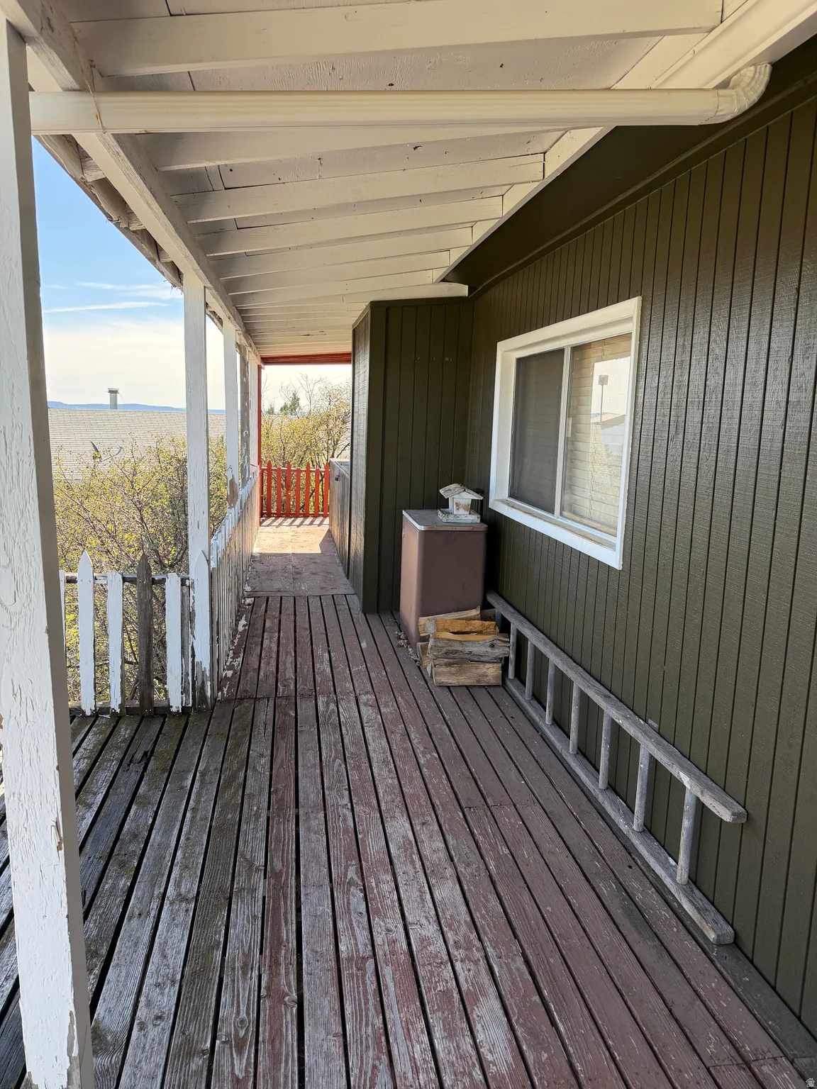 Covered wooden porch with slatted decking and a white picket fence