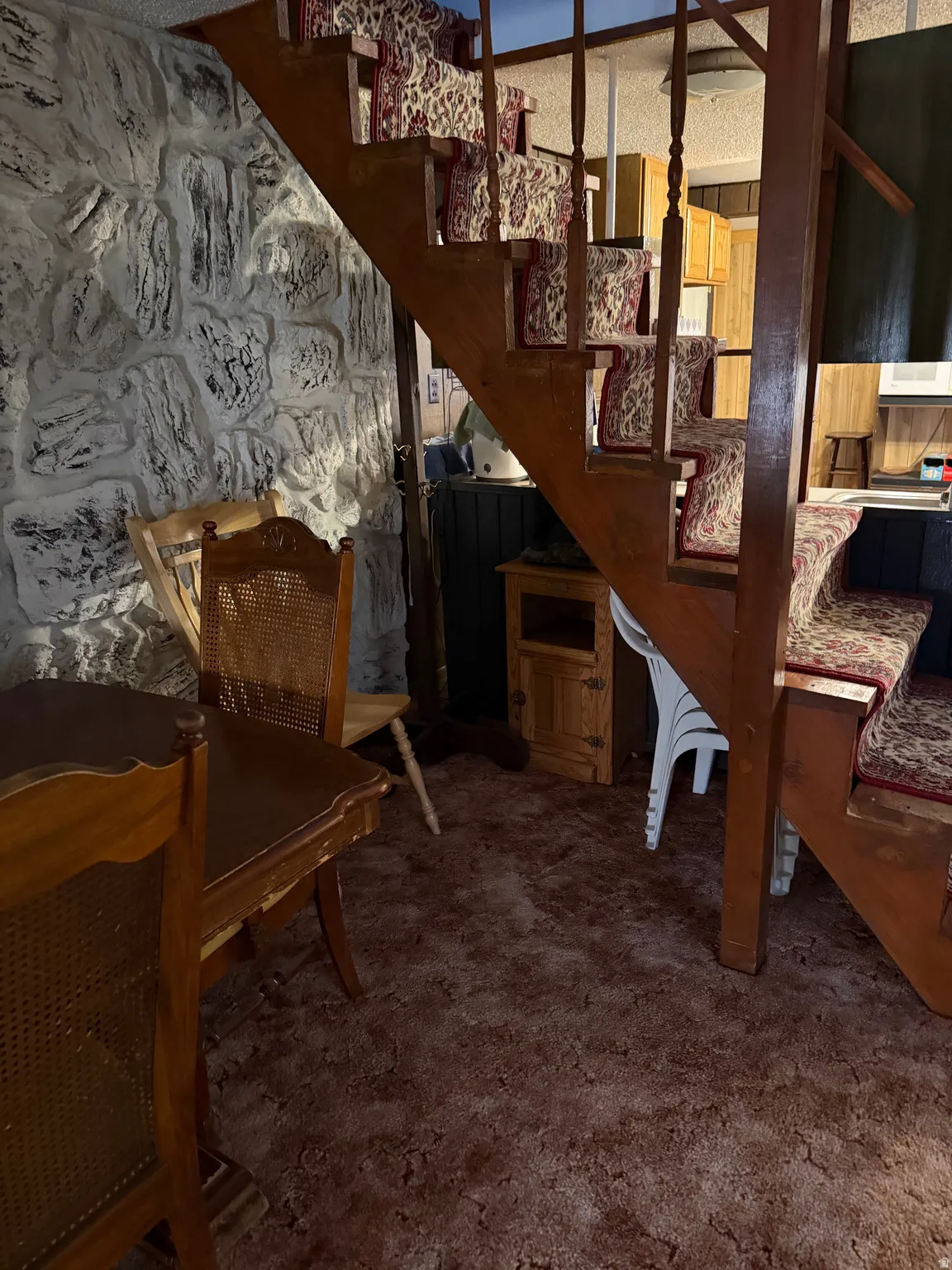 Wood staircase with patterned stair runners, stone-effect wall, and carpeted flooring