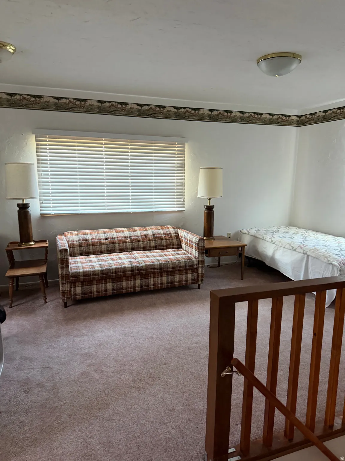 Window with blinds, wall-mounted light fixture, carpeting, wood railing