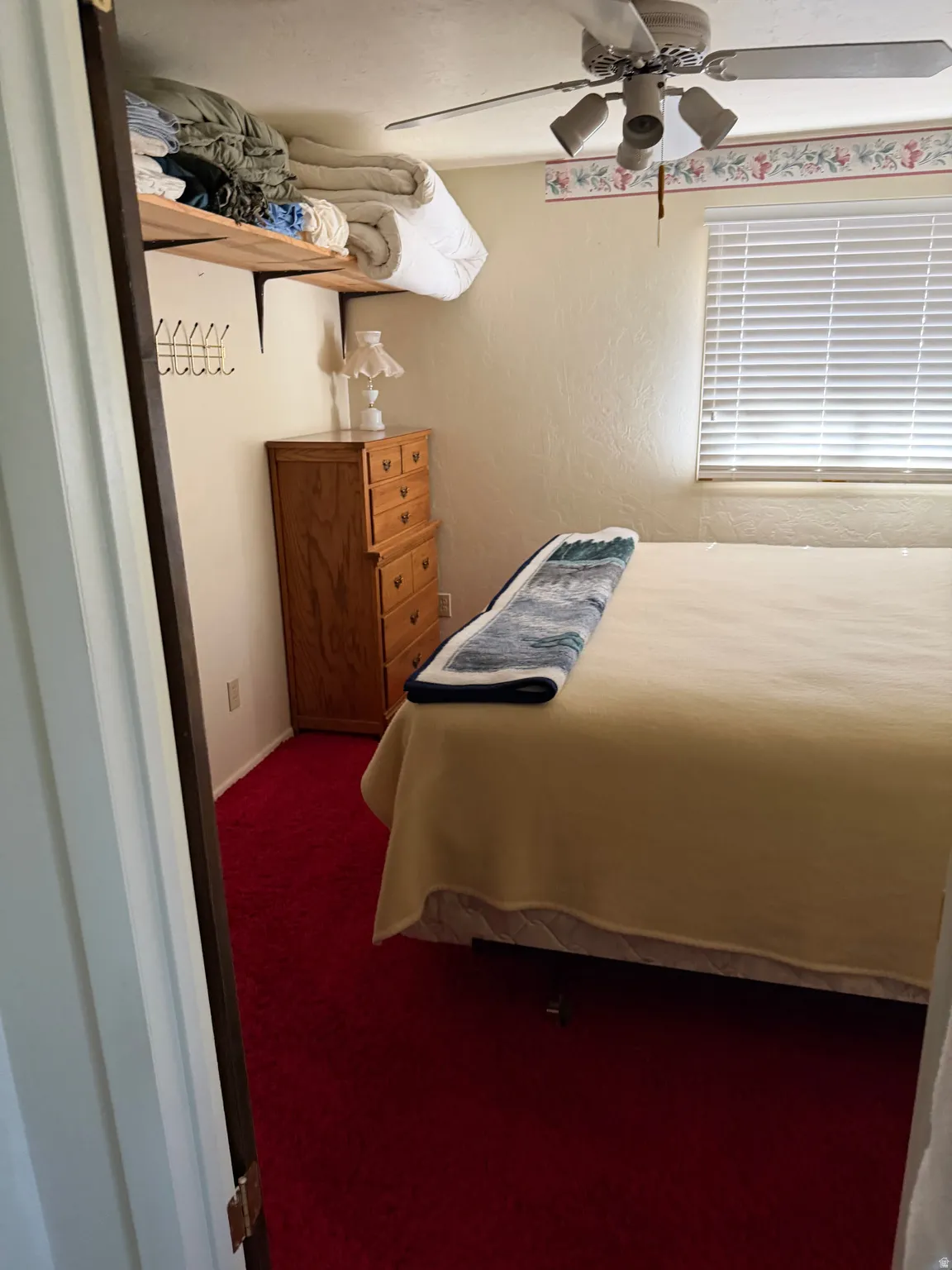 Recessed window with blinds, ceiling fan with integrated lighting, wood-finish shelving, and wall-to-wall carpeting