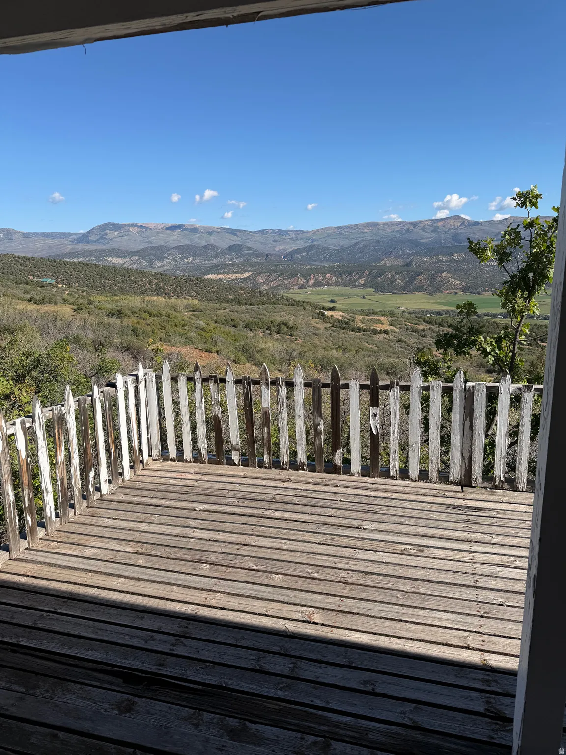 Wood-finish deck with a painted picket railing, overlooking expansive mountain and valley scenery
