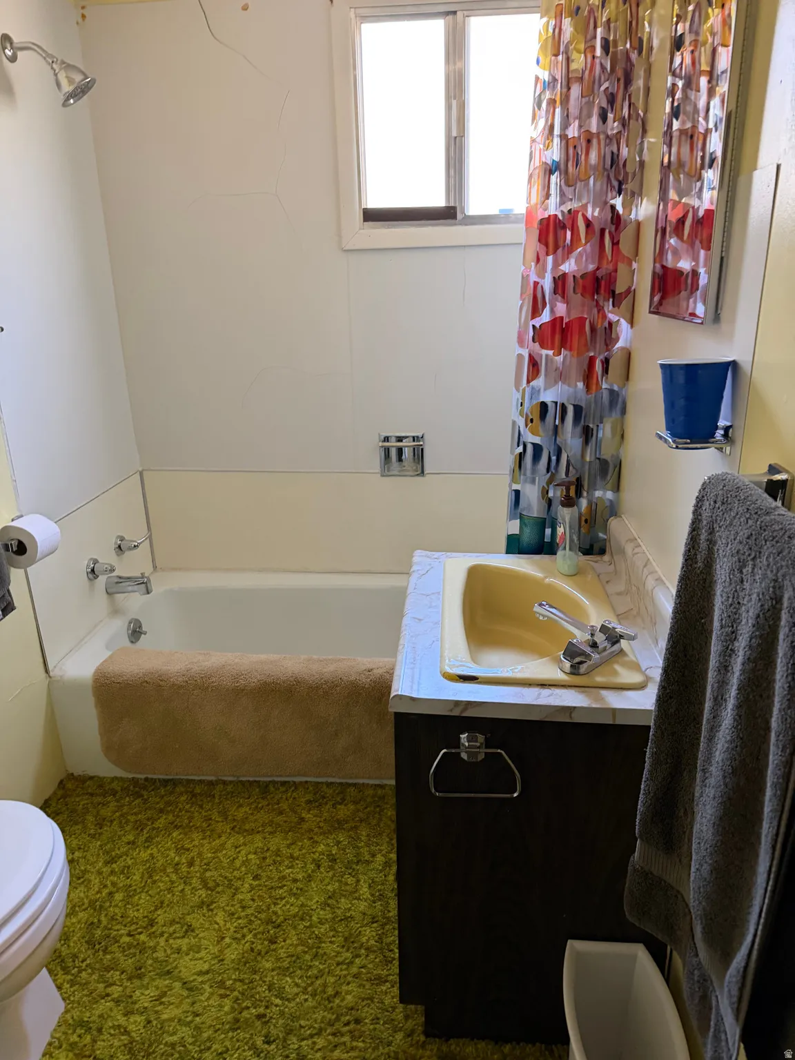 White bathtub with chrome fixtures, built-in vanity with a yellow sink and laminate countertop, and a toilet with a white tank