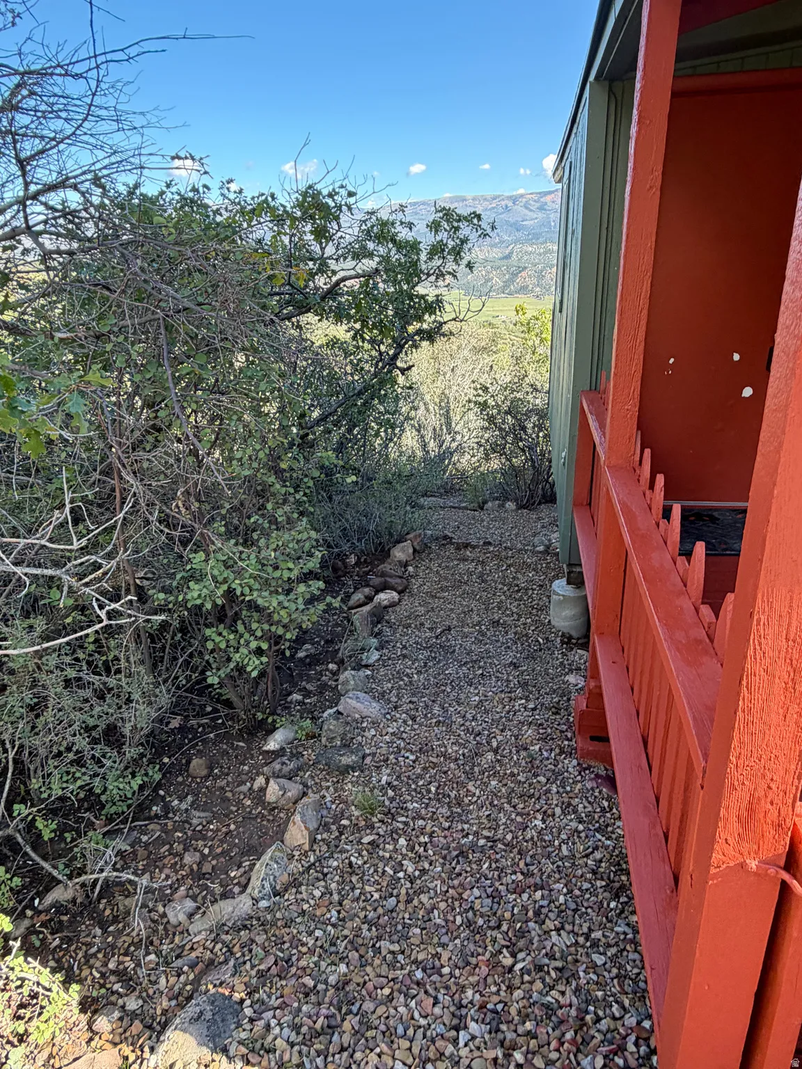 Gravel pathway with a rock border, alongside a structure with painted siding and a railing