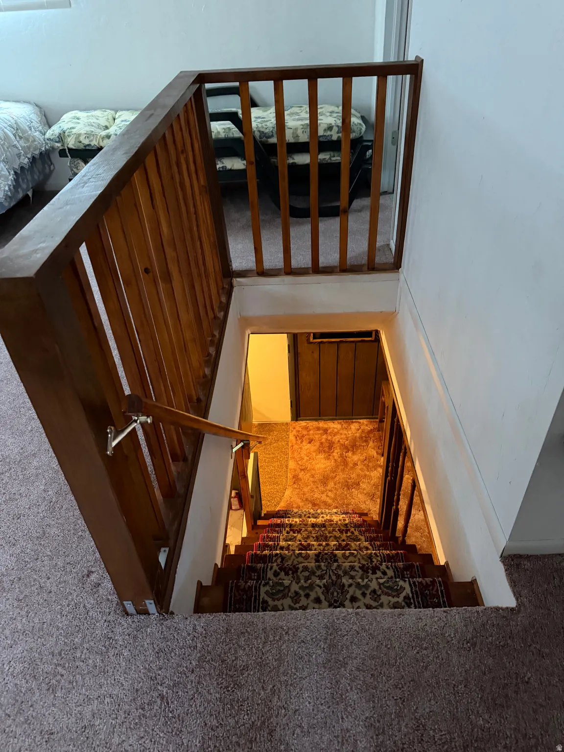 Wood-finish stair railing with matching handrail, patterned carpet on stairs, and brown carpet at the lower level