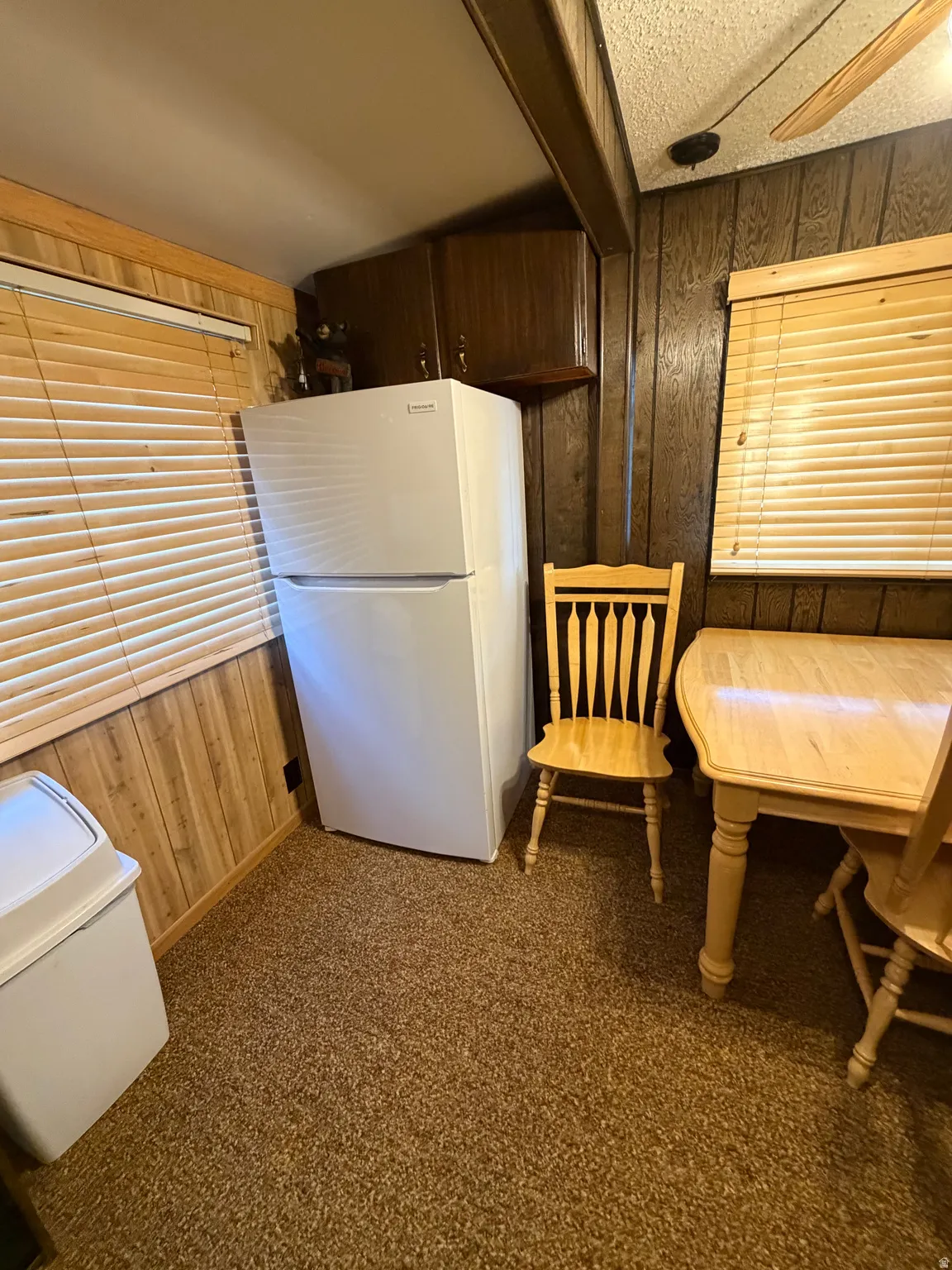 Wall paneling, white refrigerator, wood-finish cabinetry, textured ceiling, ceiling fan