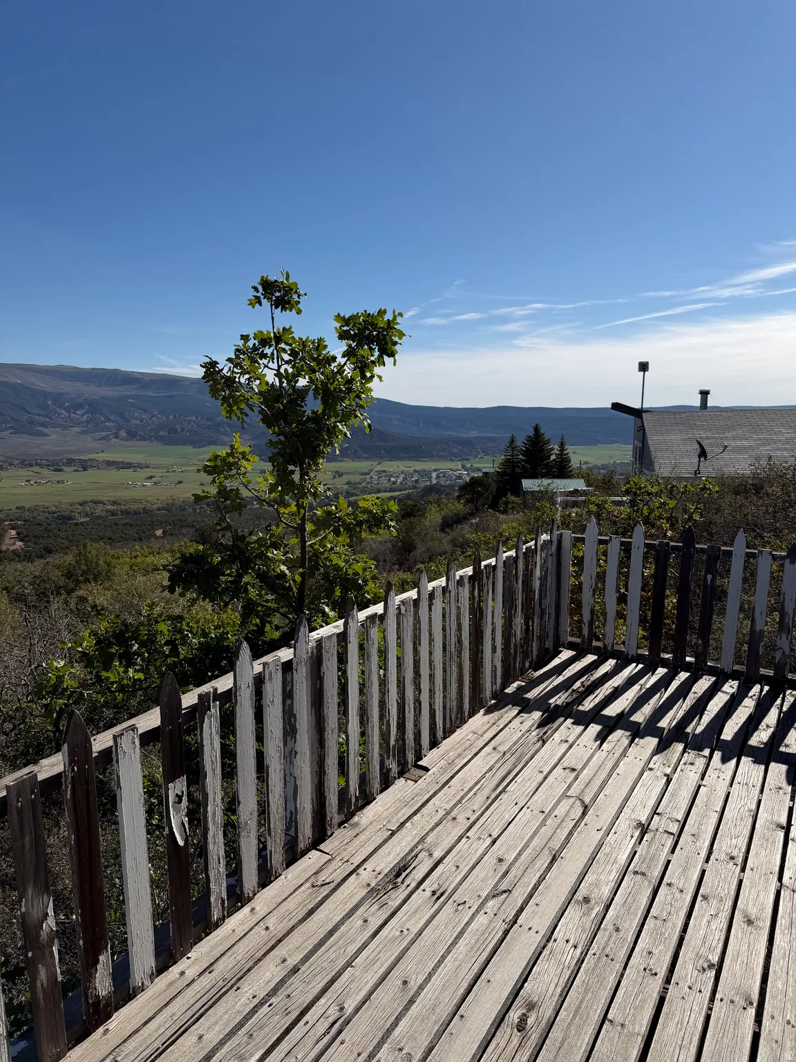 Wood-plank outdoor decking with a picket fence, surrounded by lush foliage and distant mountains