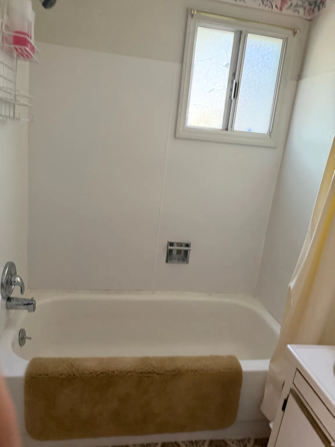 Bathtub with chrome fixtures, a built-in shower caddy, and an overhead window