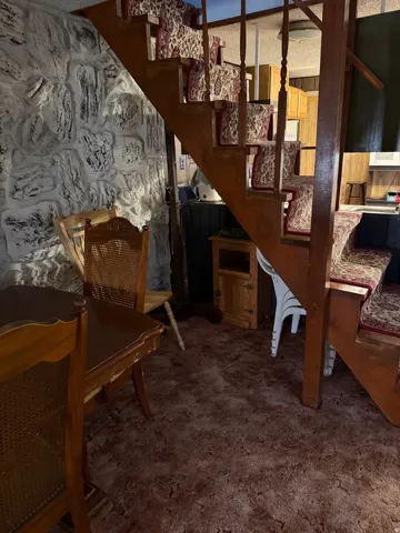 Wood staircase with patterned stair runners, stone-effect wall, and carpeted flooring