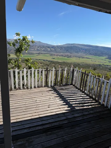 Outdoor wood-plank deck with a white picket-style railing, offering a panoramic mountain and valley backdrop